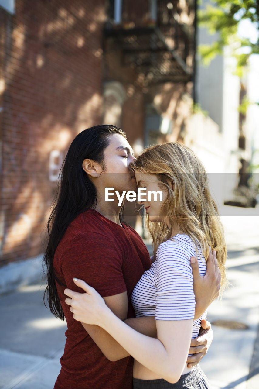 Young man embracing girlfriend while standing in city