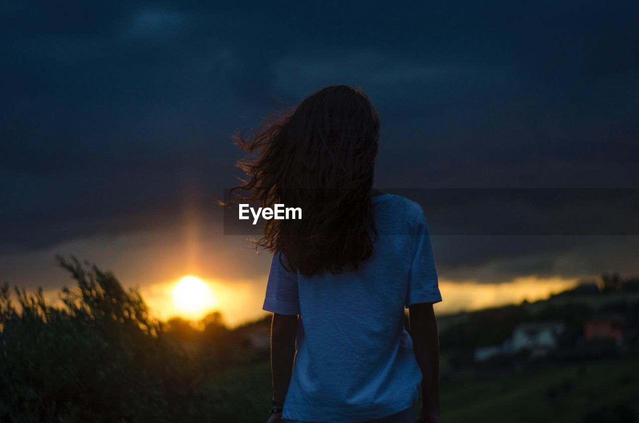 Rear view of woman standing against sky during sunset