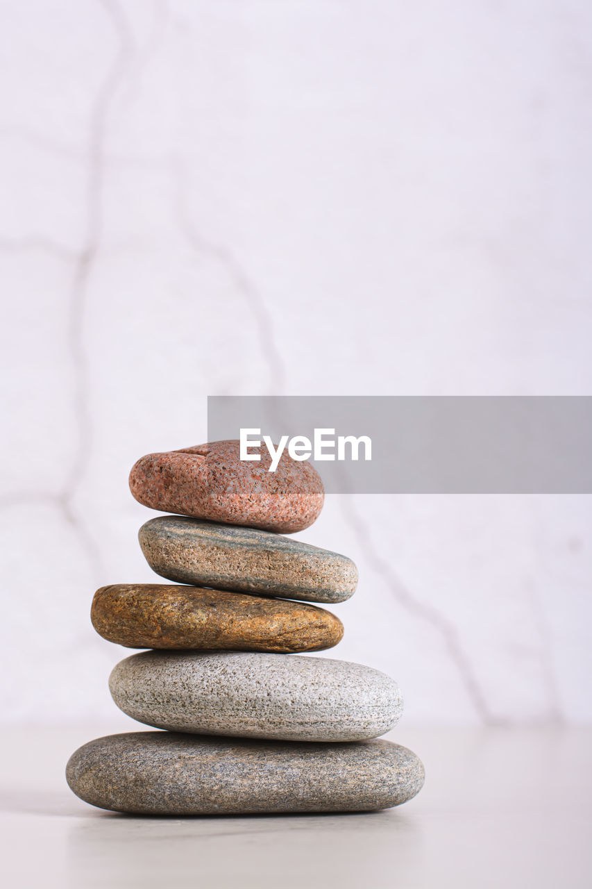 Pyramid of smooth sea stones on a table on the background of a plastered wall vertical view