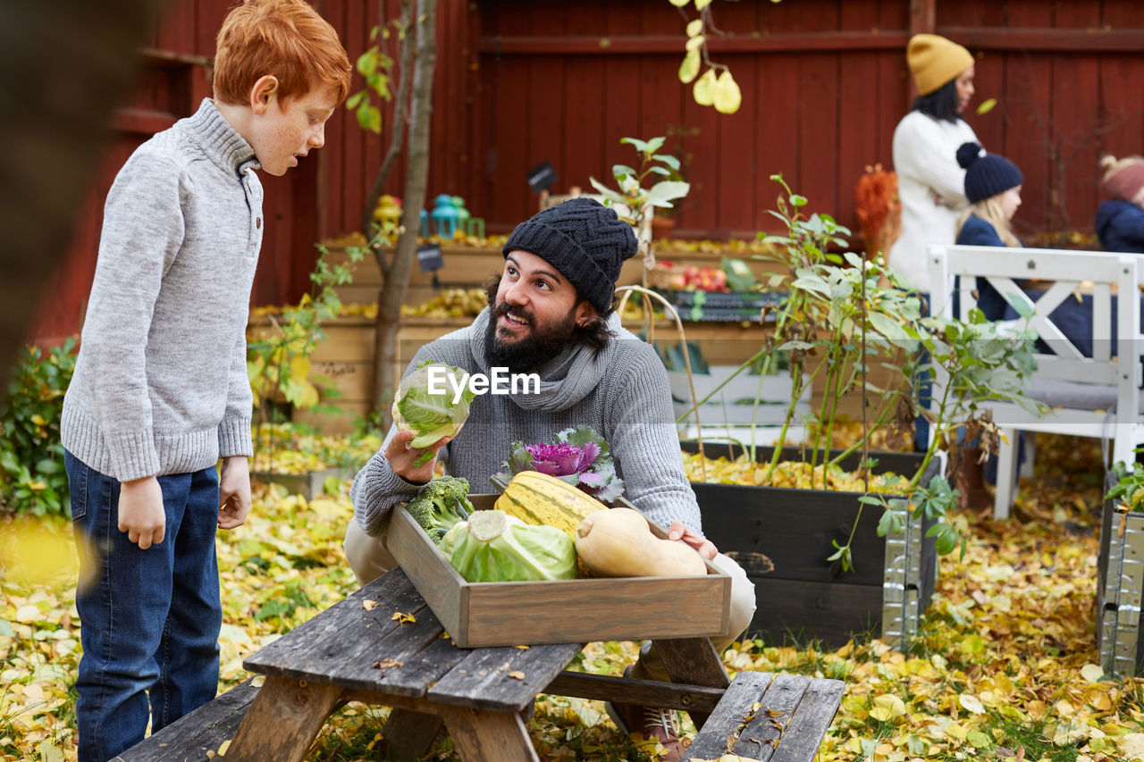 Man talking to boy while holding cabbage at table in yard