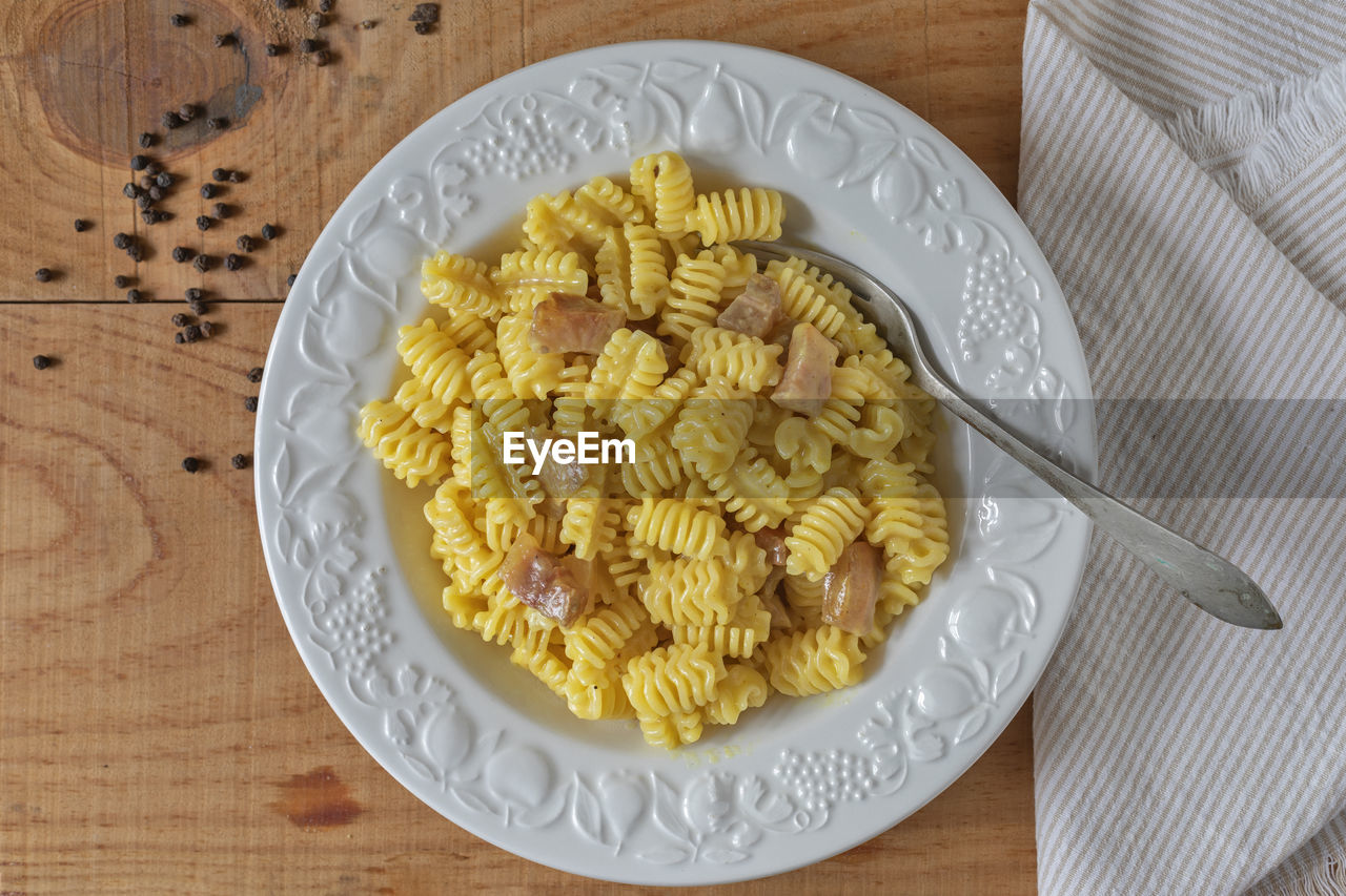 A plate of pasta carbonara on a wooden board. on the side, whole black peppercorns.