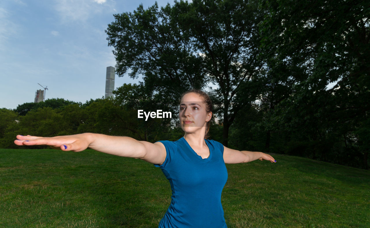 YOUNG WOMAN WITH ARMS RAISED STANDING ON FIELD