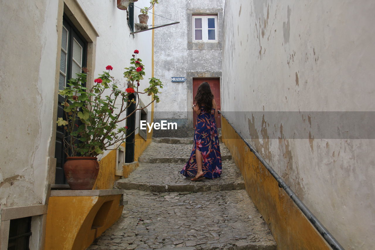 REAR VIEW OF WOMAN WALKING ON ALLEY AMIDST BUILDING