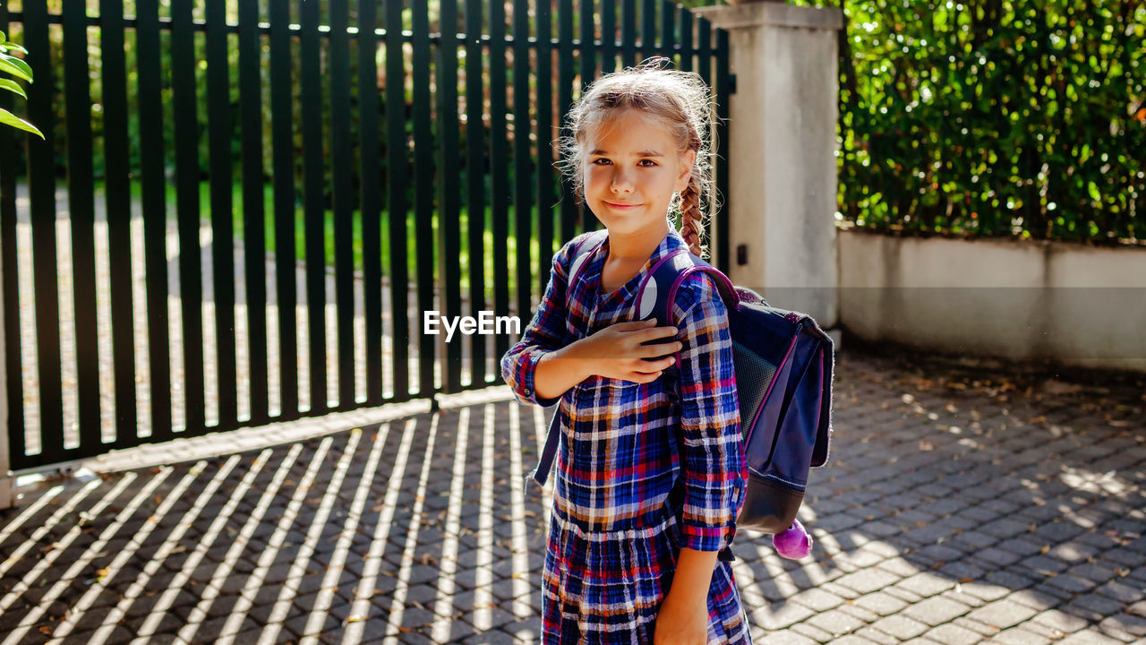 Girl with backpack ready to school and stands with hand on her heart at first day after vacation