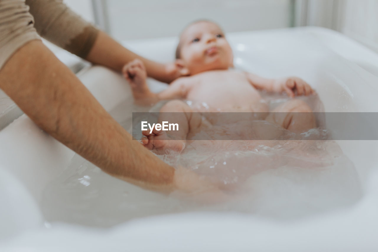 Close-up of father holding baby girl in bathtub at bathroom