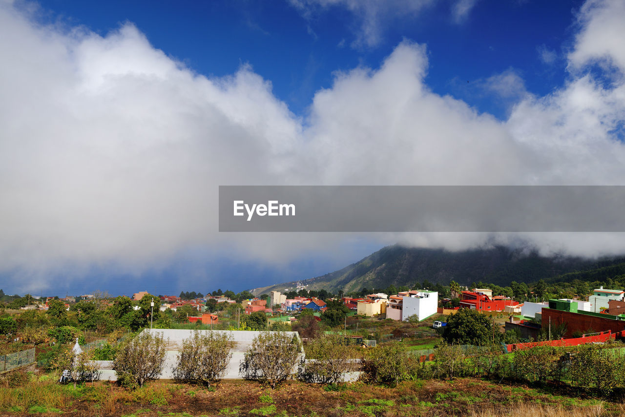 Scenic view of clouds over town at mountain against blue sky