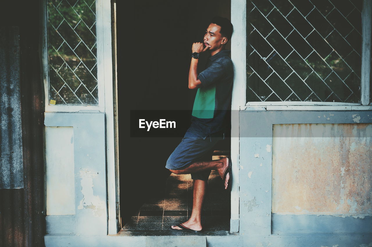 Side view of thoughtful man looking away while standing on doorway in house