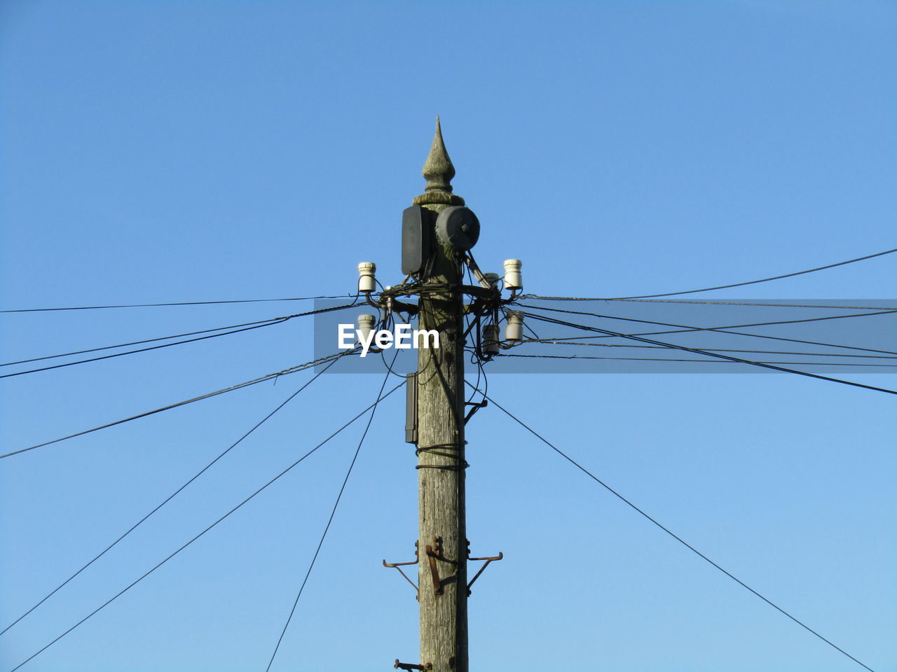 Power lines on pole against clear blue sky