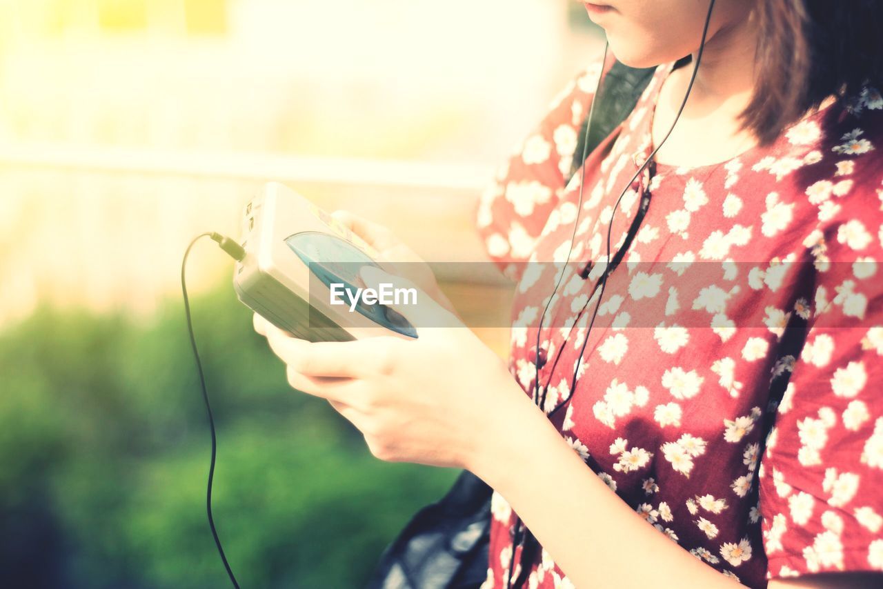 Midsection of woman listening music through personal cassette player