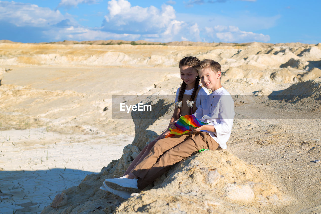 A boy and a girl collect kite sitting on a stone on a sunny summer day.