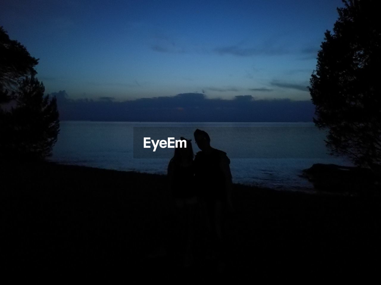 Silhouette couple at beach against sky