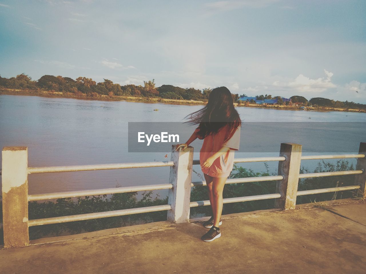 Woman standing on bridge by lake against sky