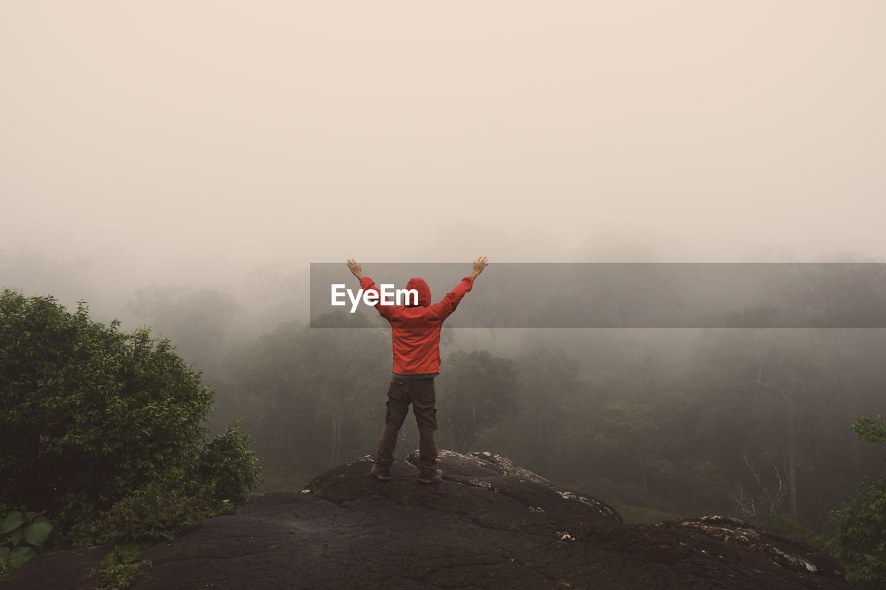 Rear view of man standing on mountain during foggy weather