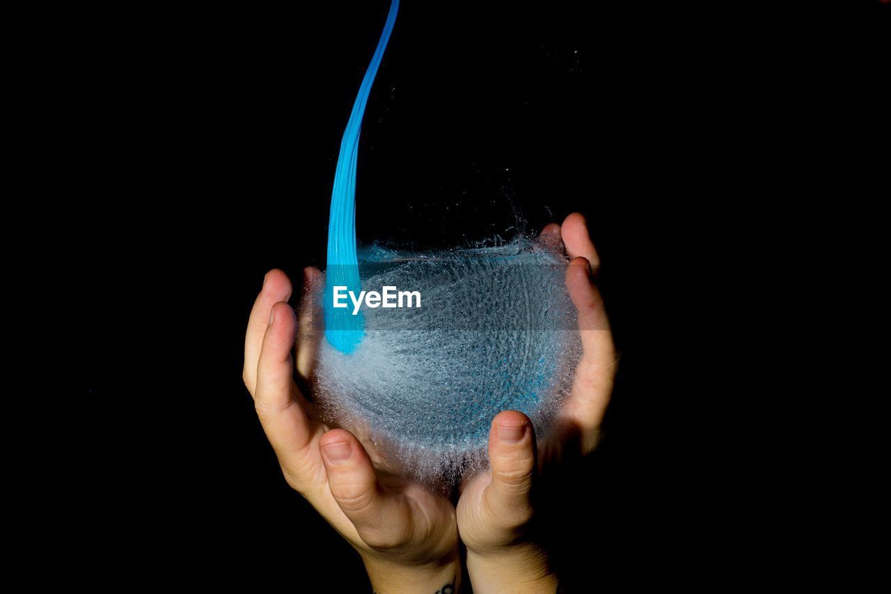 Cropped hands holding bursting water balloon against black background