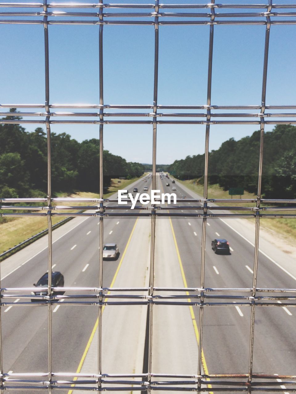 Cars on road against clear sky seen through fence