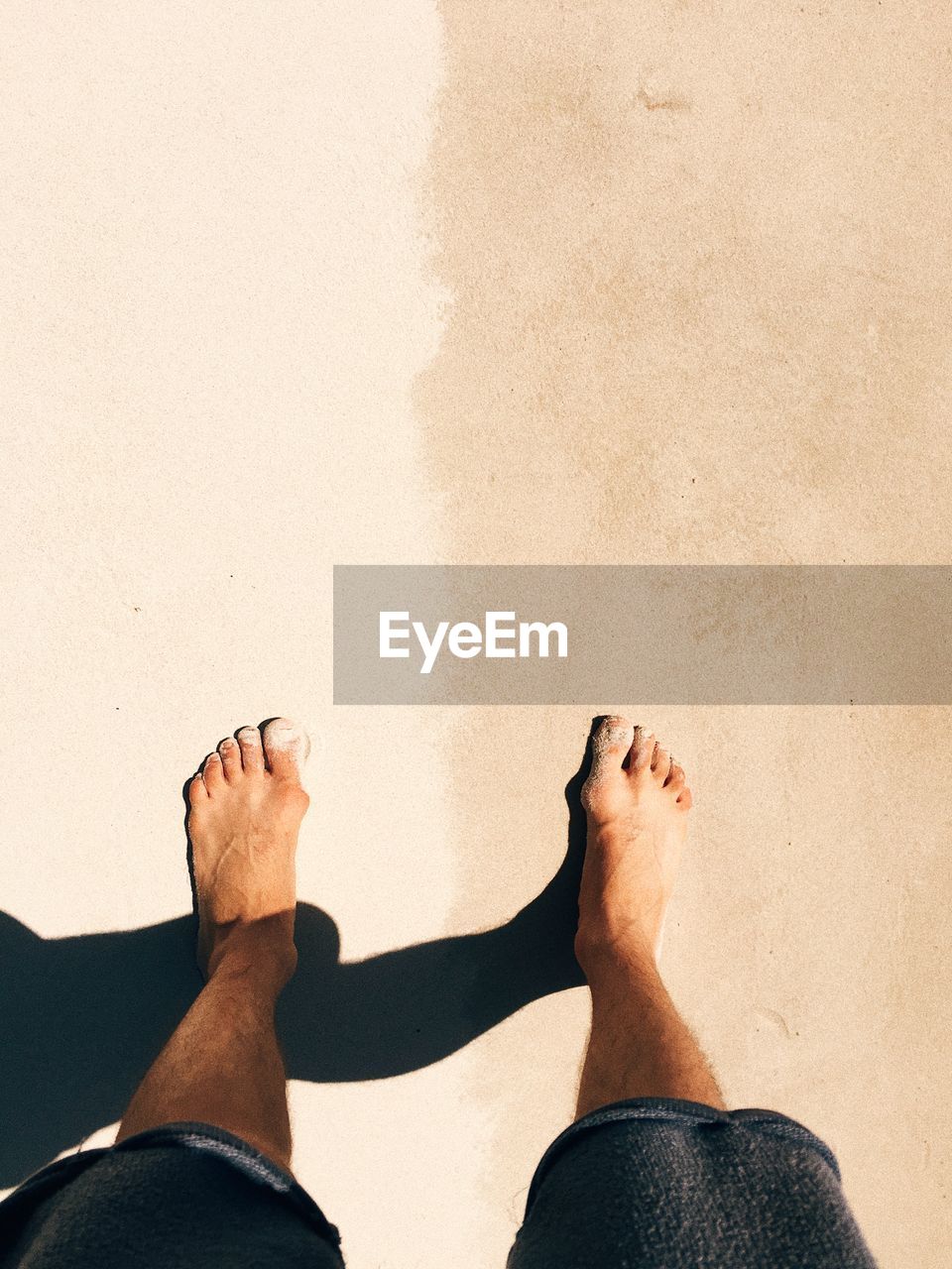 Low section of man standing on sand during sunny day