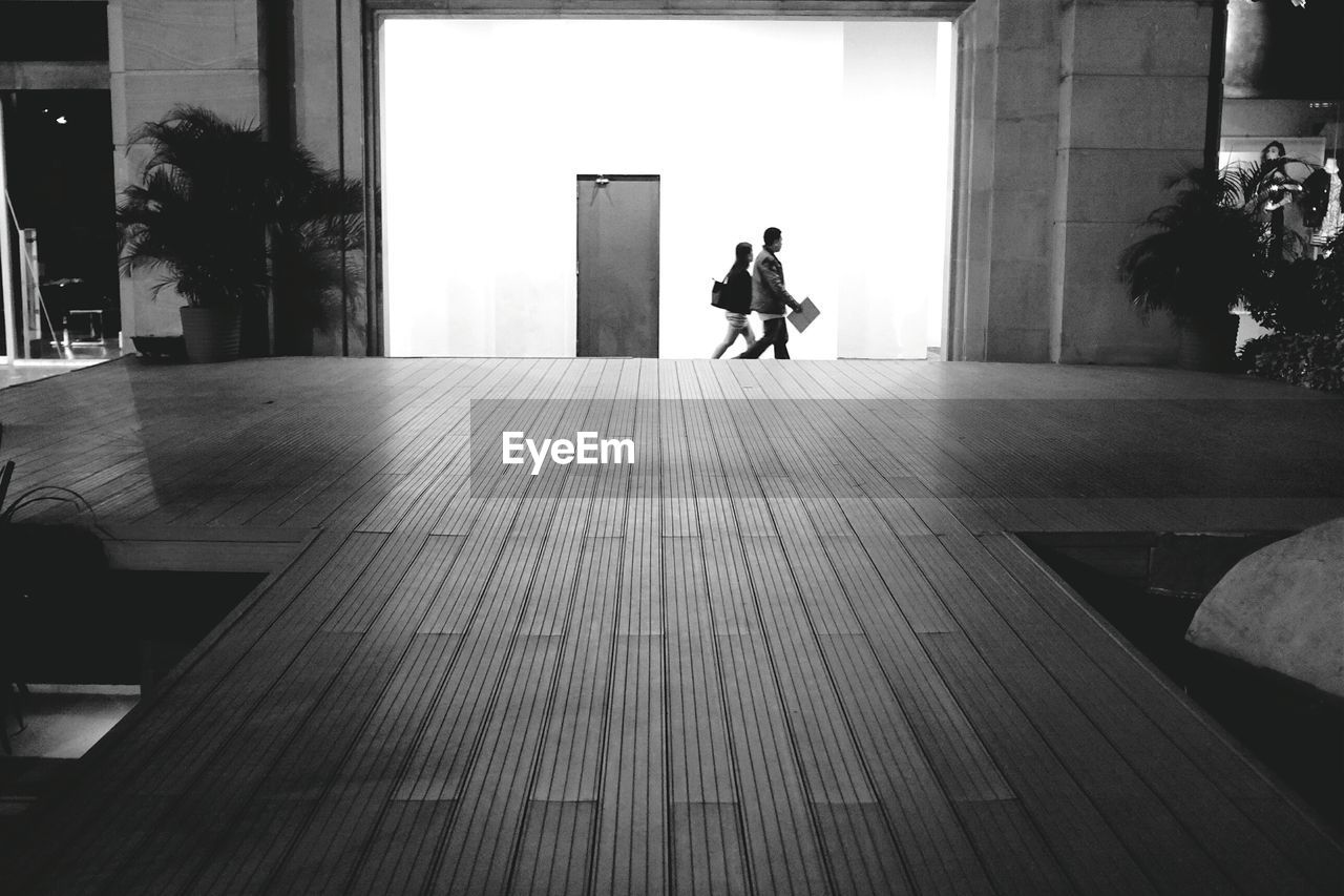 Man and woman walking on street seen through building