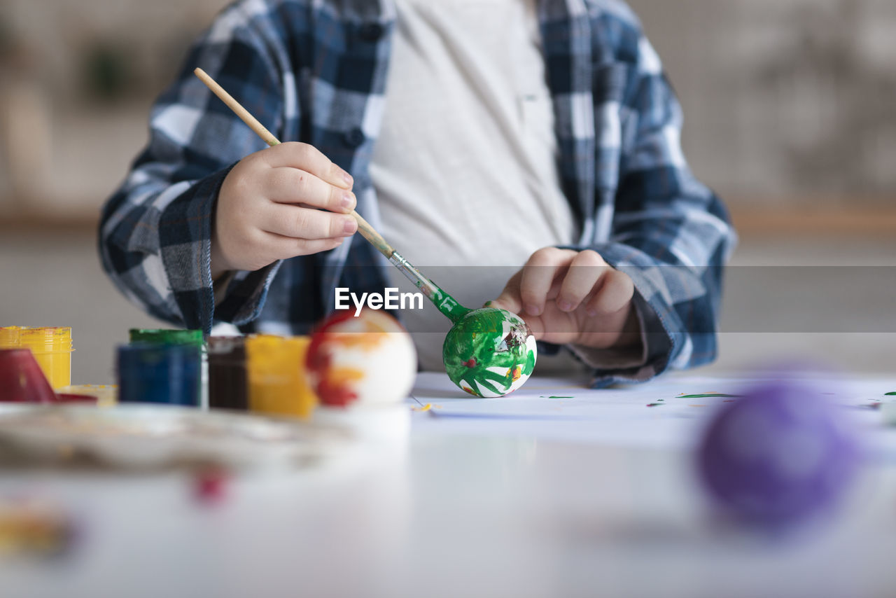 Midsection of boy painting easter egg