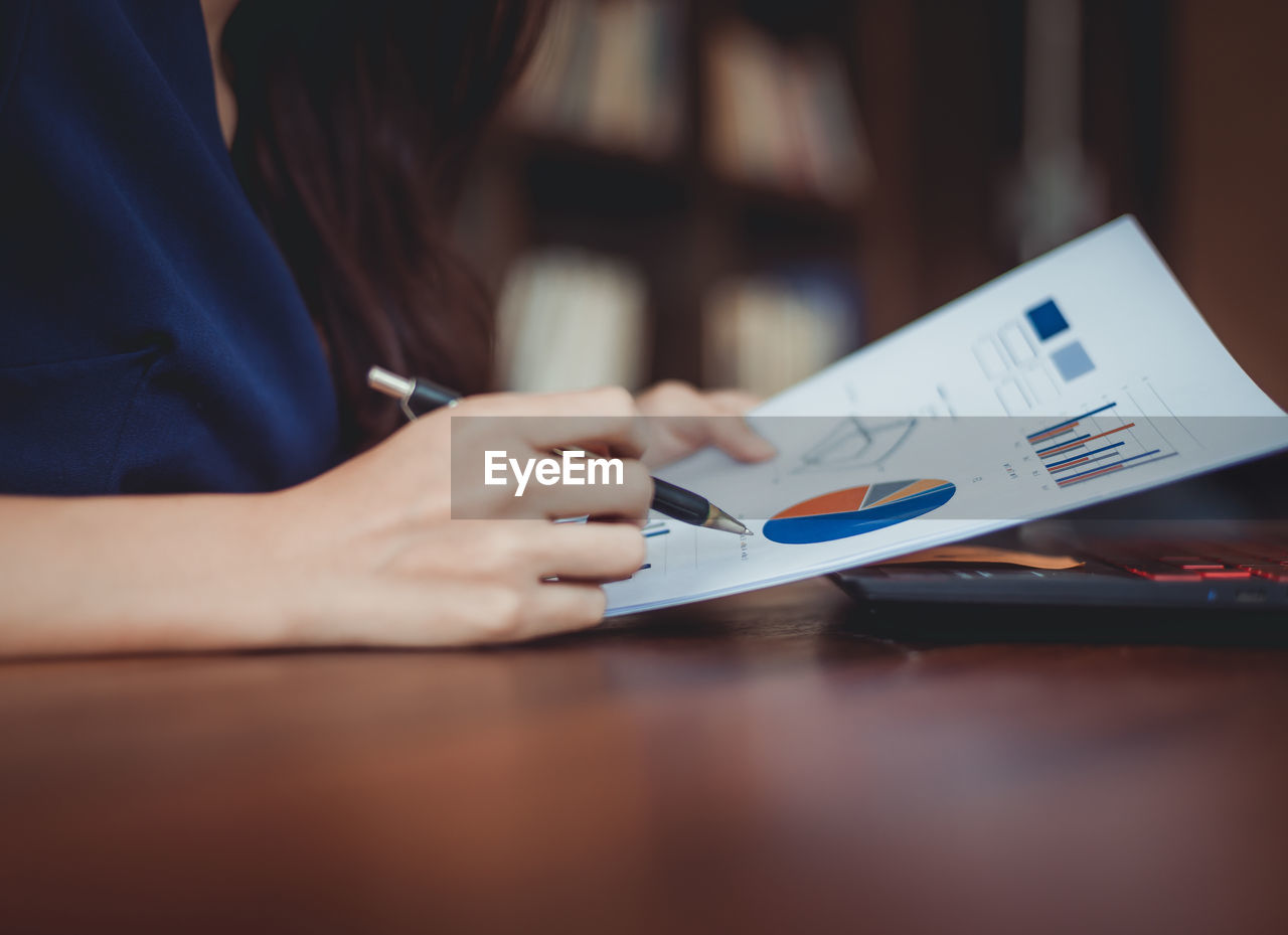 Midsection of businesswoman analyzing pie chart on paper