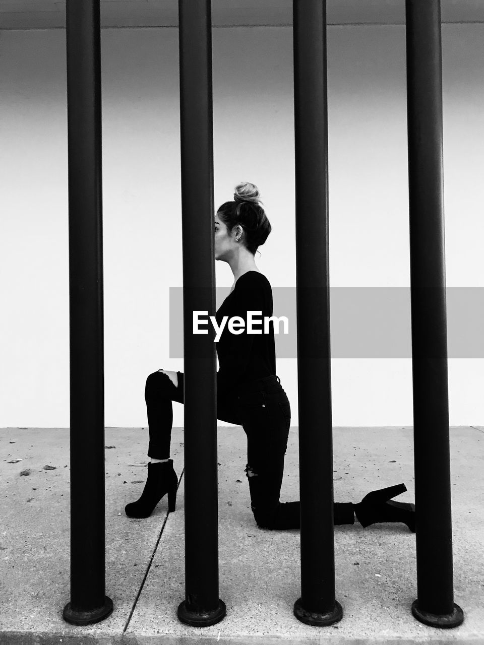 Young woman kneeling seen through prison bars