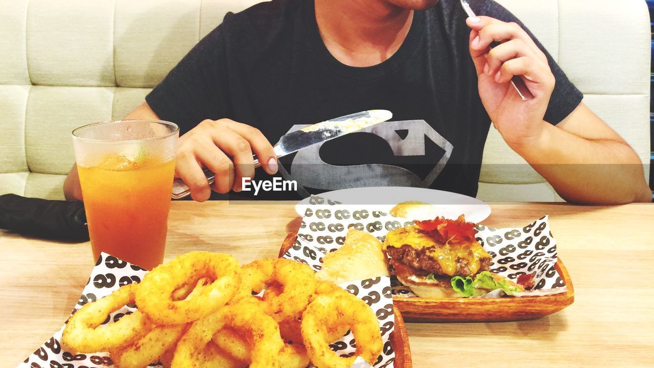 Woman eating burger and onion rings in restaurant