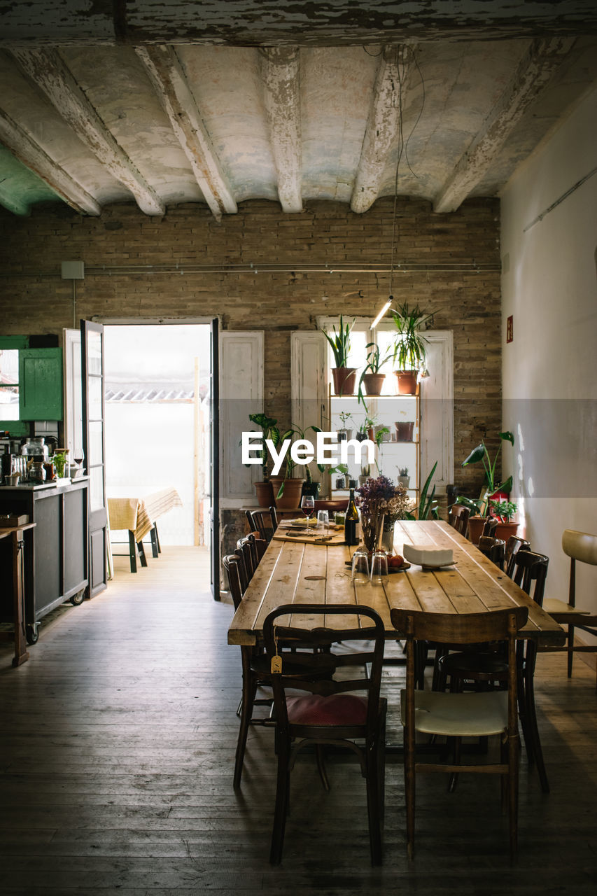 Large wooden table and chairs in rustic retro styled bar with shabby ceiling and potted green plants on window