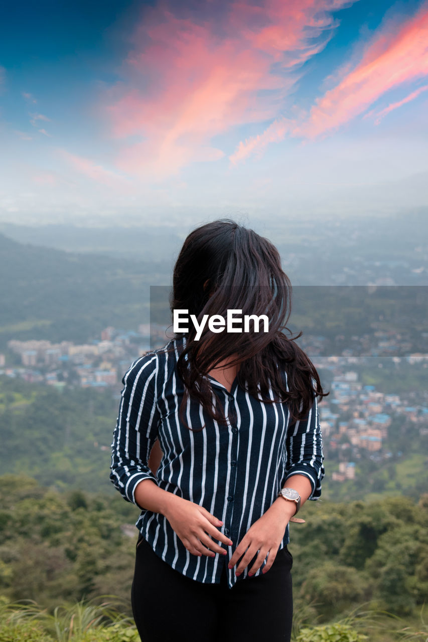 Woman with tousled hair standing on mountain against sky