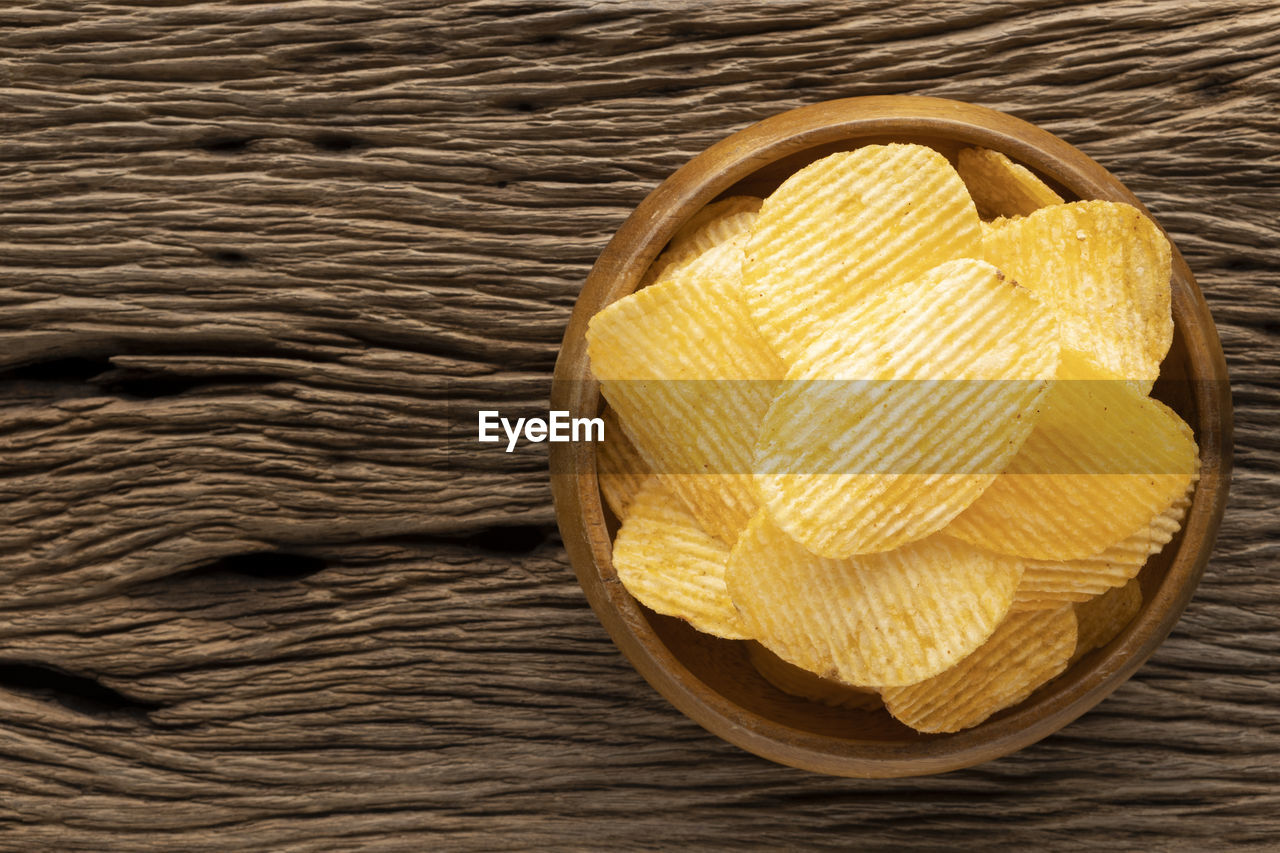 Tasty ridged potato chips in wooden bowl on rustic wood with copy space for text, tone, top view