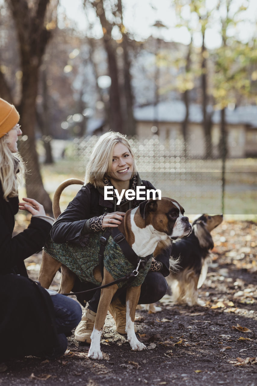 Portrait of smiling blond woman crouching by friend with dogs at park