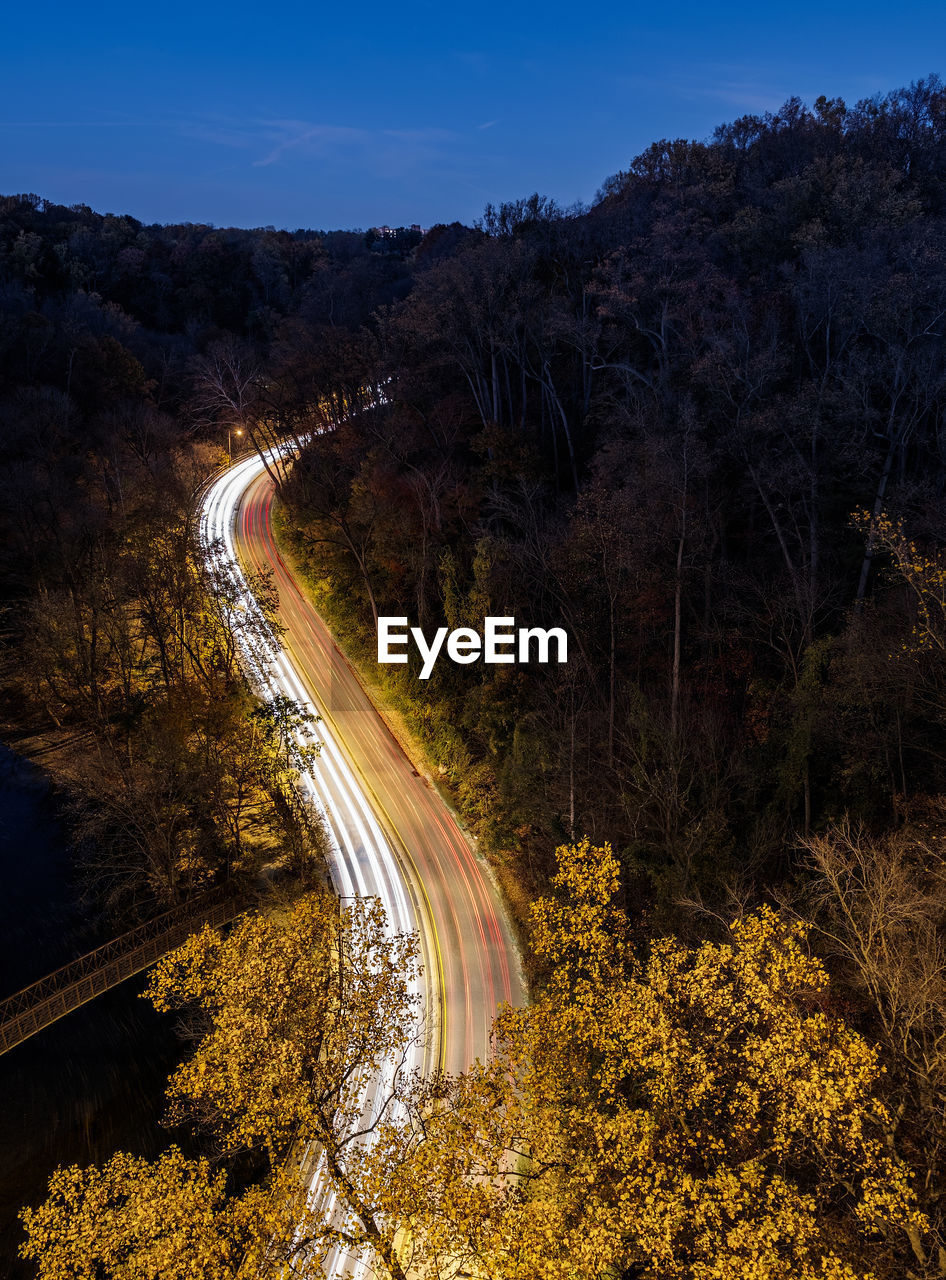 HIGH ANGLE VIEW OF LIGHT TRAILS ON ROAD AGAINST SKY