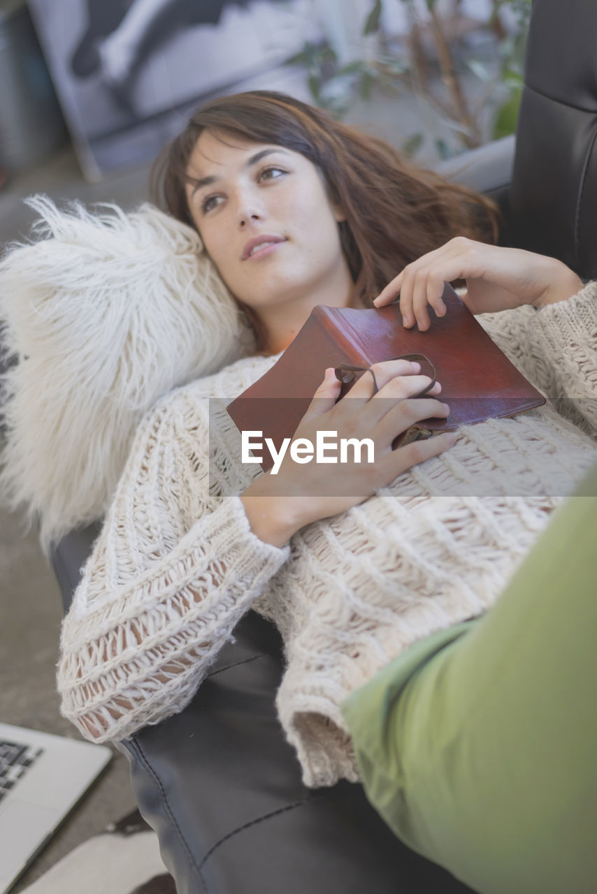 High angle view of woman with book relaxing on sofa at home