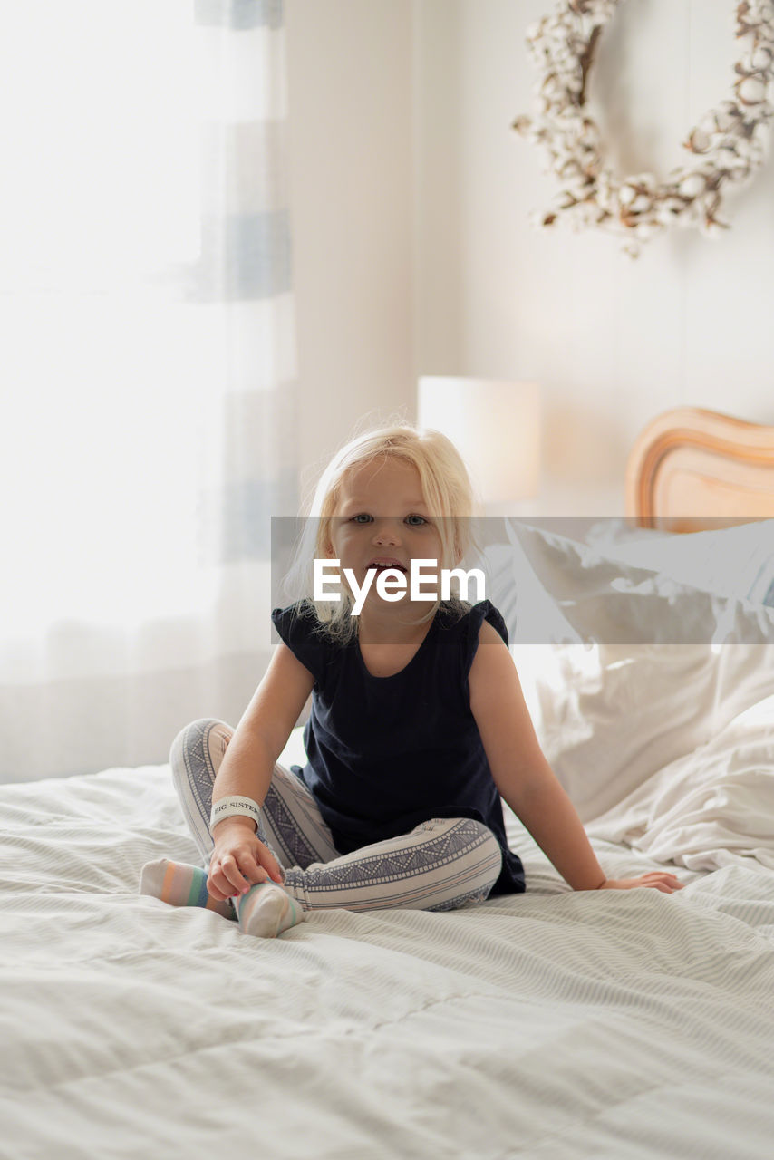 Full length portrait of girl sitting on bed at home