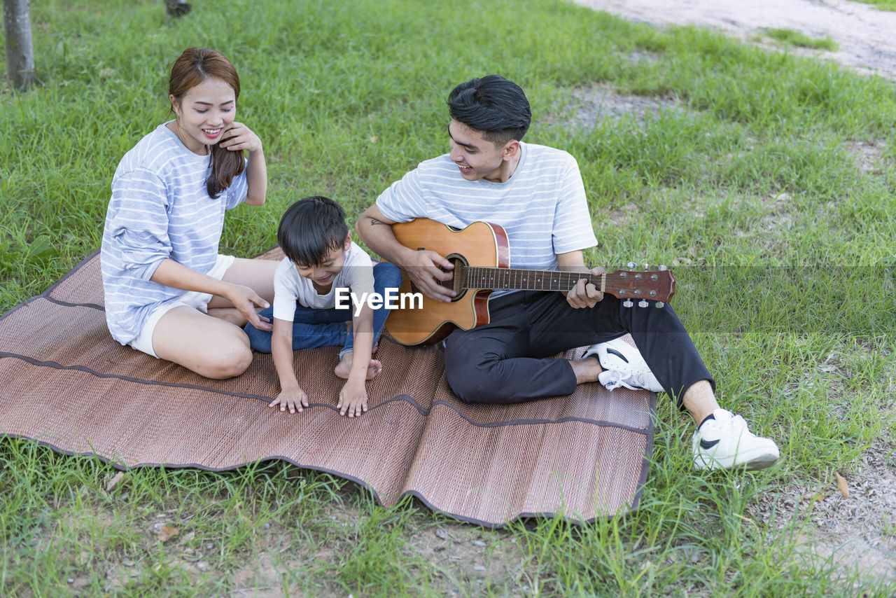 side view of young woman using mobile phone while sitting on field