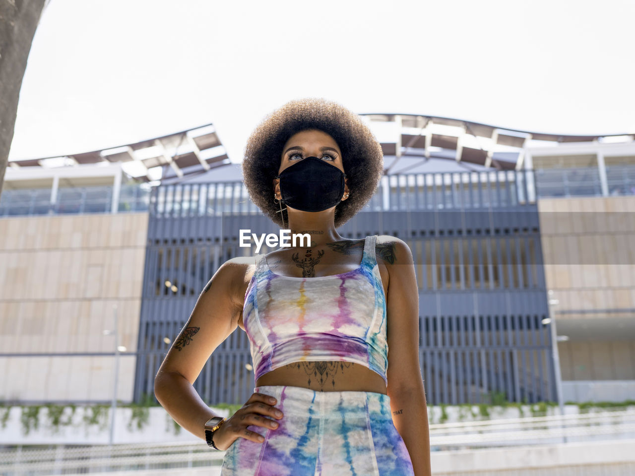 Confident african american female in medical mask and fashionable summer outfit standing in urban area in city during coronavirus outbreak