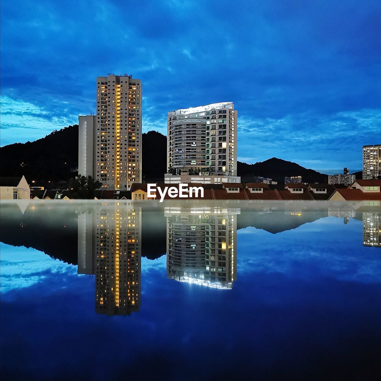 Reflection of illuminated buildings in swimming pool against sky