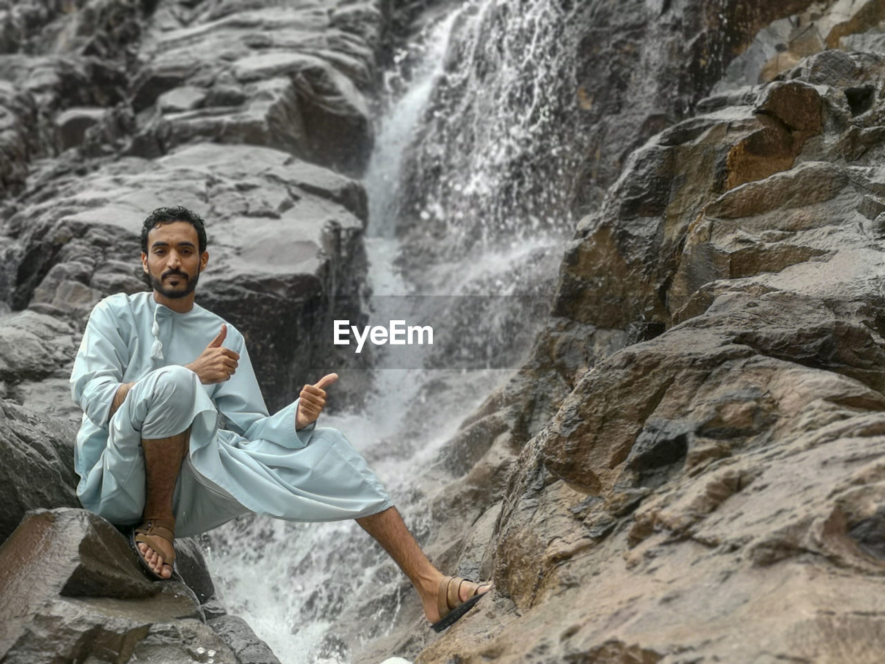 FULL LENGTH OF MAN SITTING ON ROCK AT SHORE