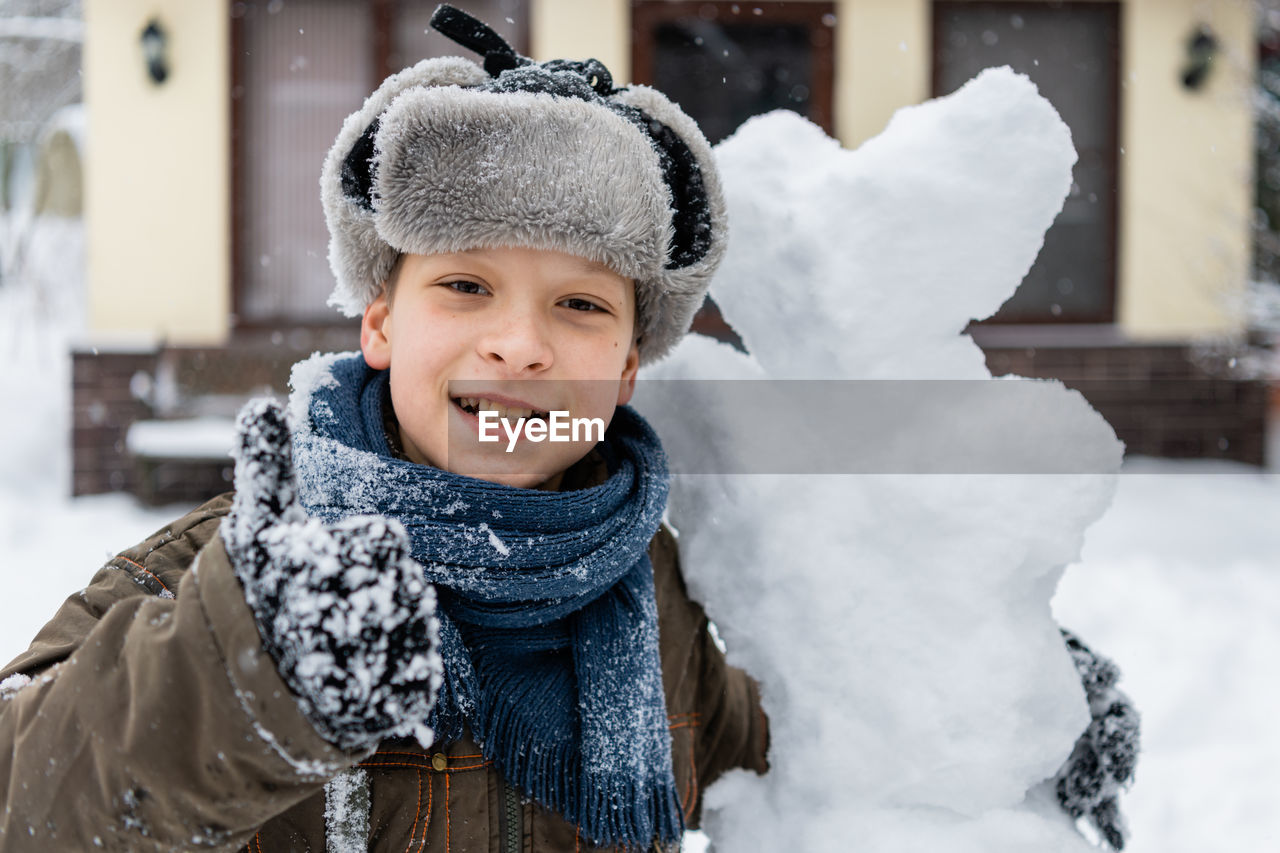 Portrait of smiling boy with snowman during winter