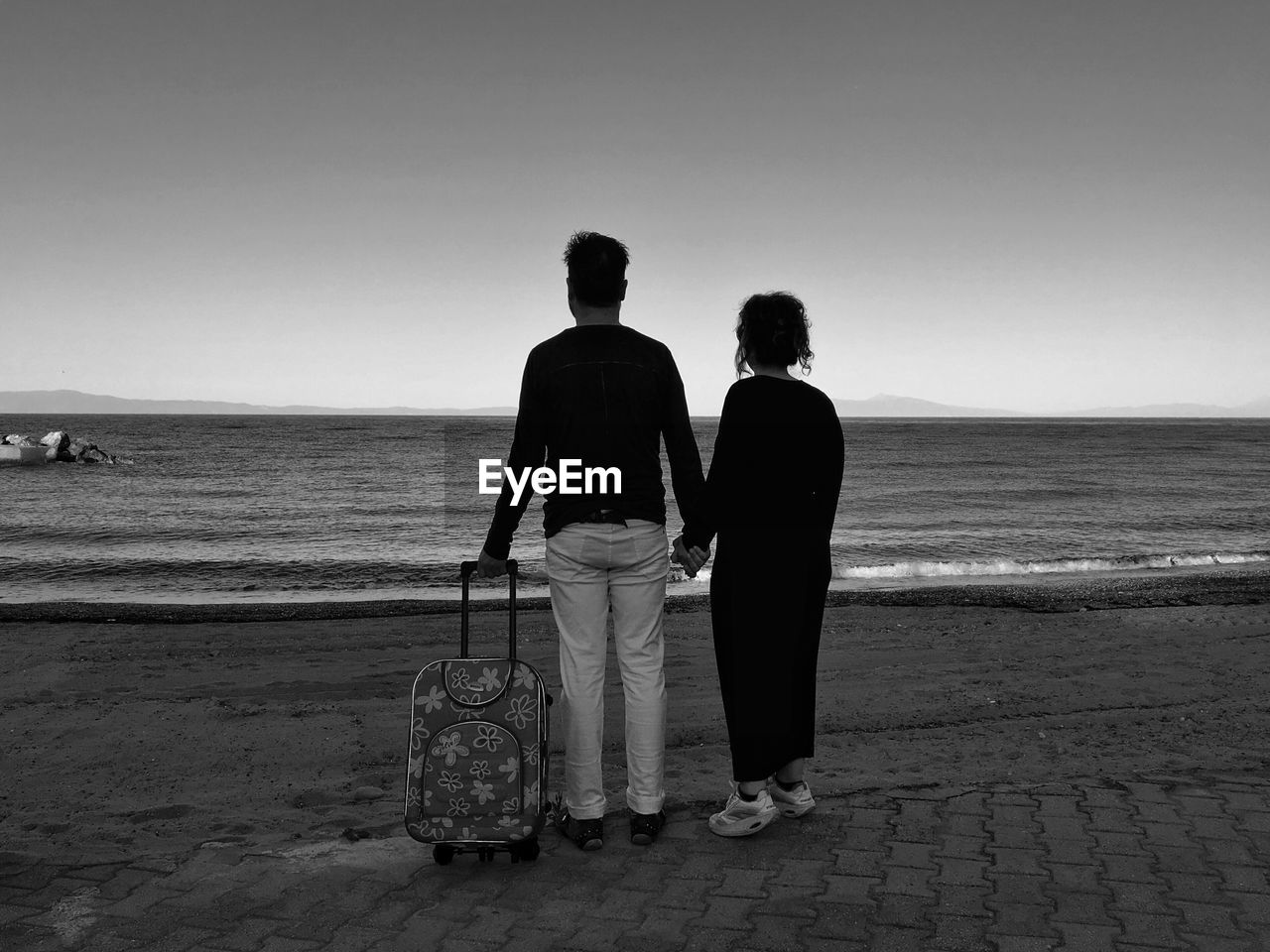 Couple with luggage standing at beach against 