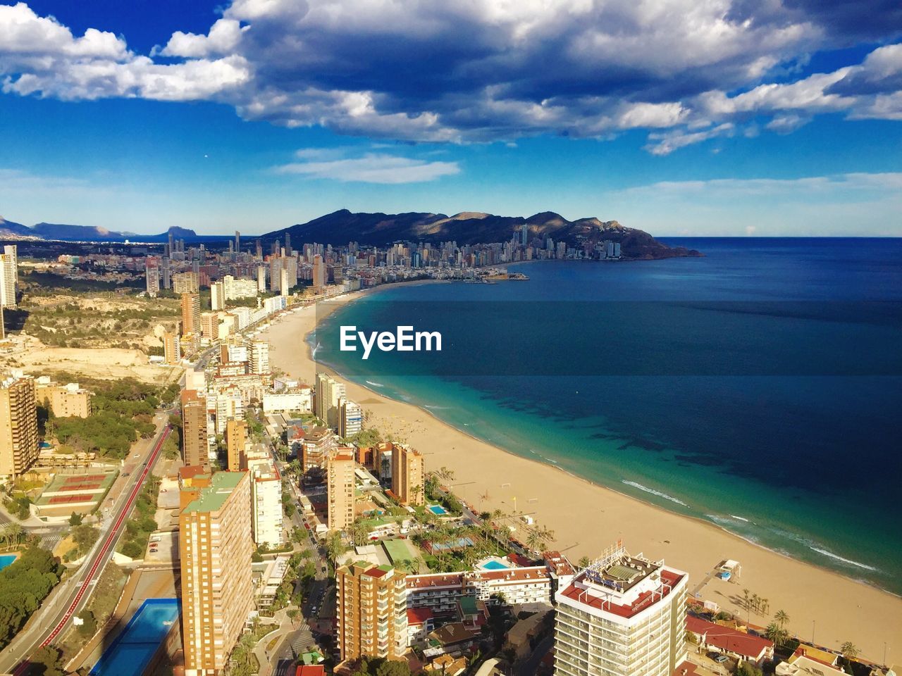 Aerial view of cityscape and sea against cloudy sky