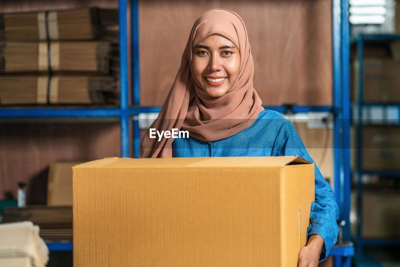 Portrait of smiling young woman holding cardboard box