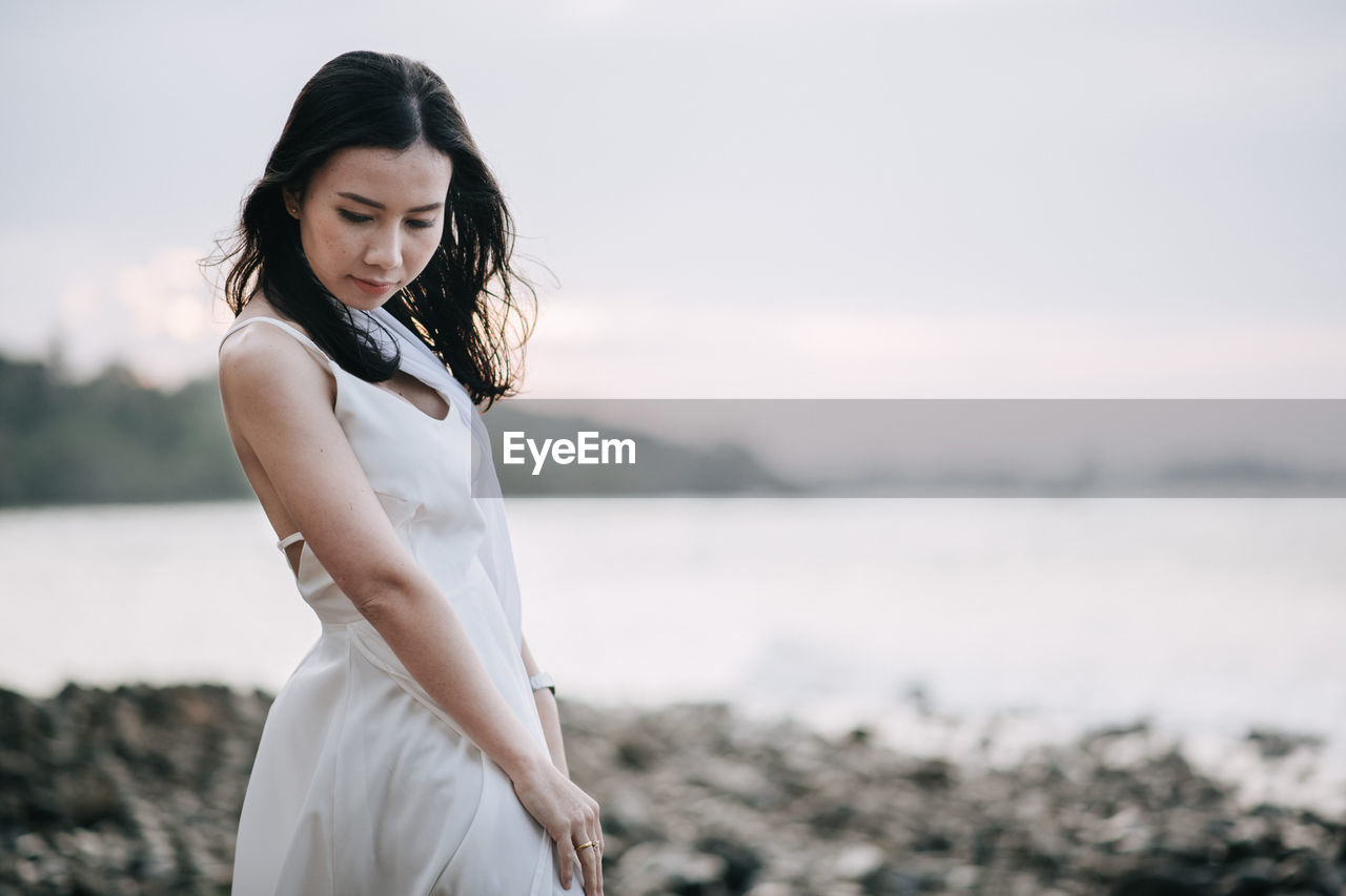 Young woman looking away while standing at beach during sunset