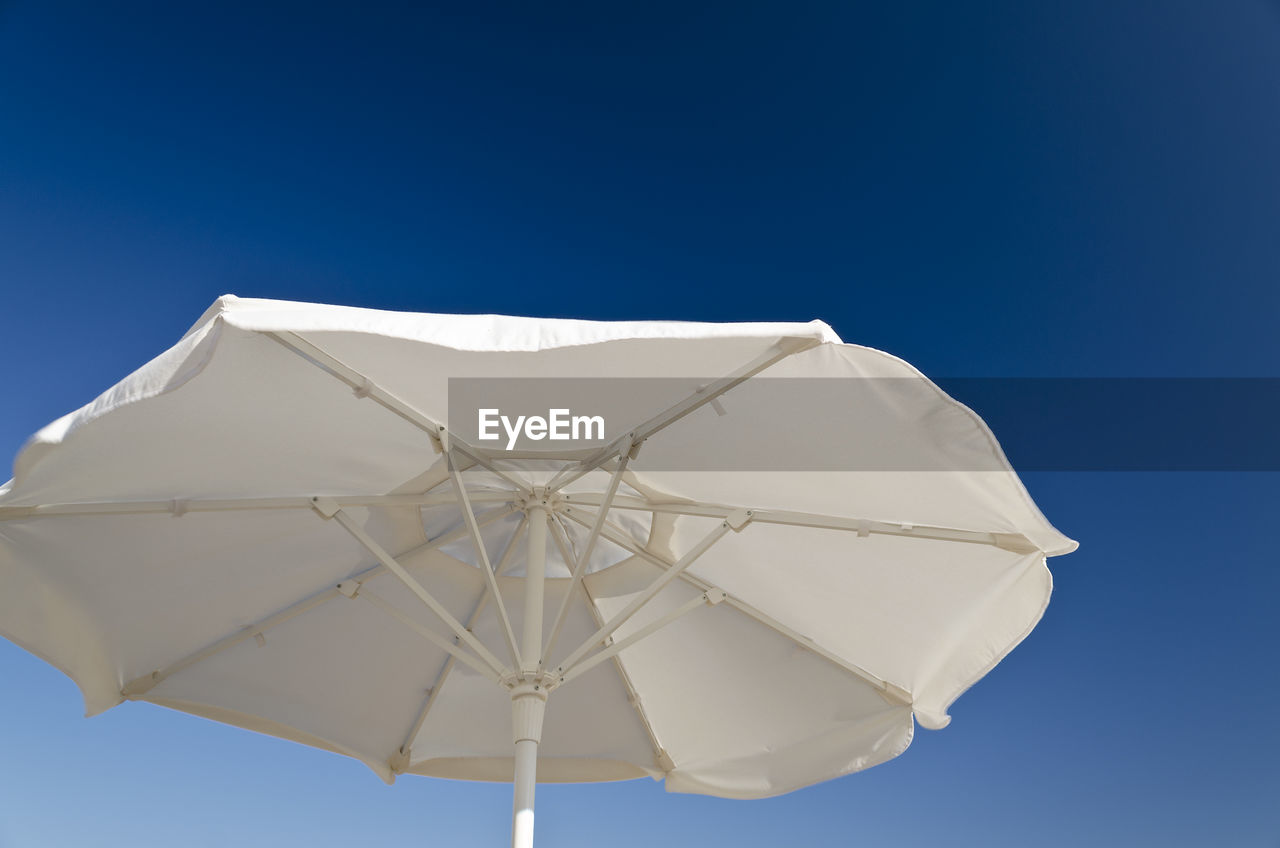 LOW ANGLE VIEW OF WHITE UMBRELLA AGAINST BLUE SKY