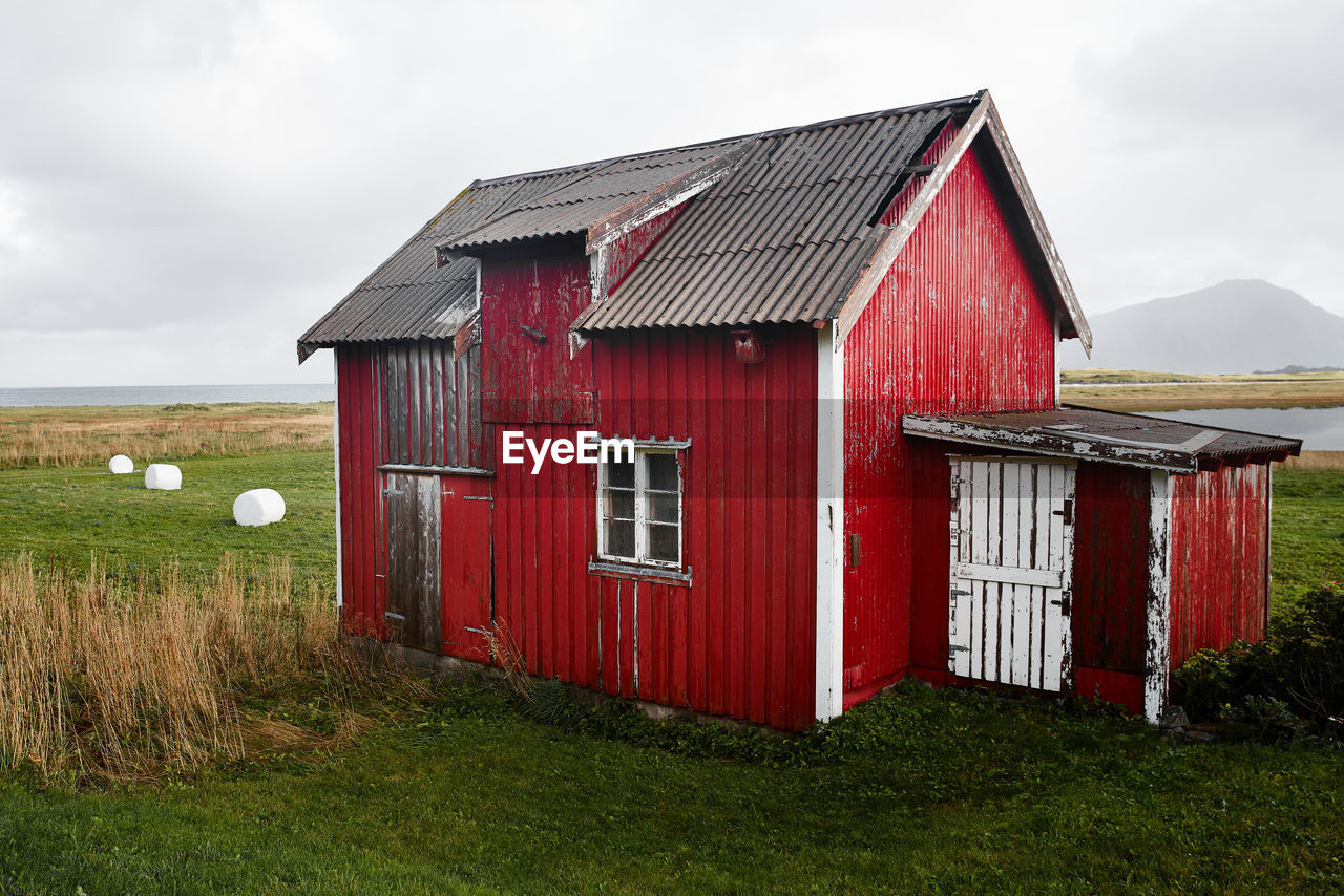 Barn on field by building against sky