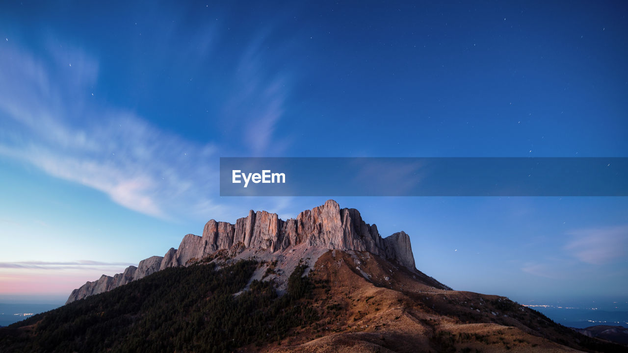 Twilight panoramic mountain view, starry sky and clouds, city lights in the background