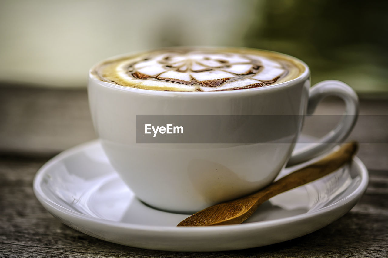 A cup of hot coffee with latte art, serving on dark wooden table in natural day light