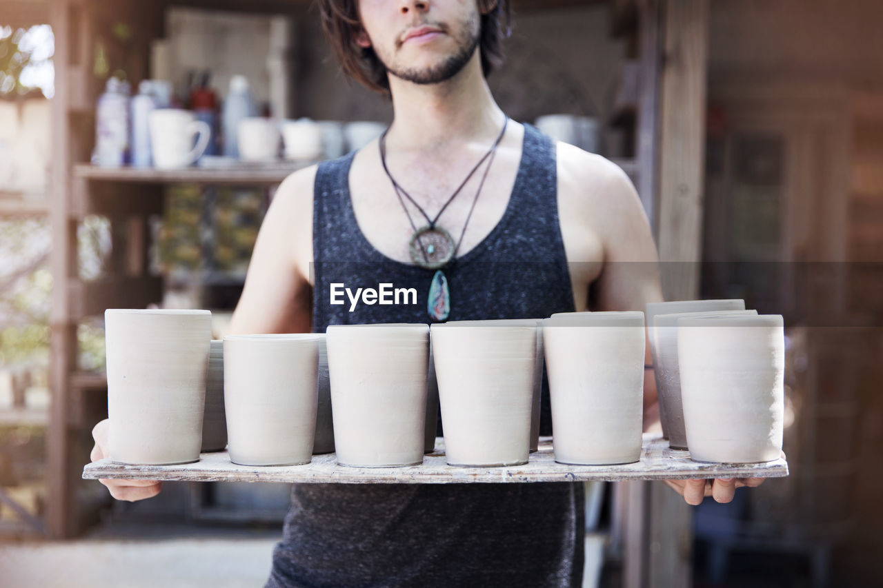 Midsection of craftsman holding clay containers at workshop