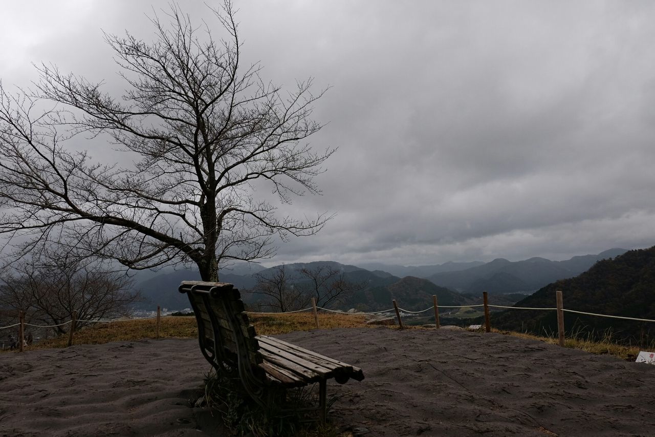 Empty bench on mountain against cloudy sky