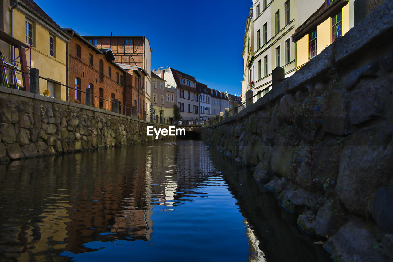 Canal amidst buildings against blue sky