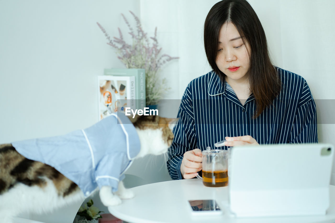 Woman in pajamas cloth drink tea and play with her cat