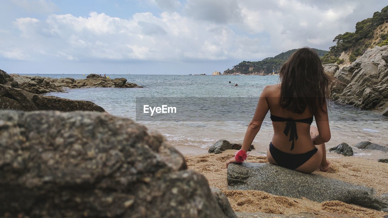 Rear view of woman sitting on beach against sky